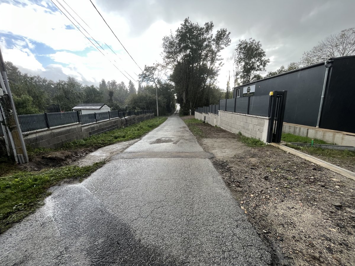 Clôture aluminium anthracite sur muret béton longeant une voie d'accès, avec portail noir et bâtiment industriel