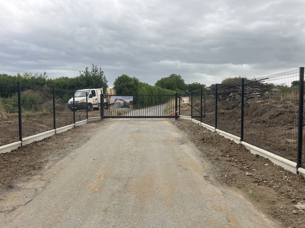 Portail autoportant coulissant noir en position fermee, encadre par une cloture rigide a panneaux noirs montee sur longrines beton, acces de chantier