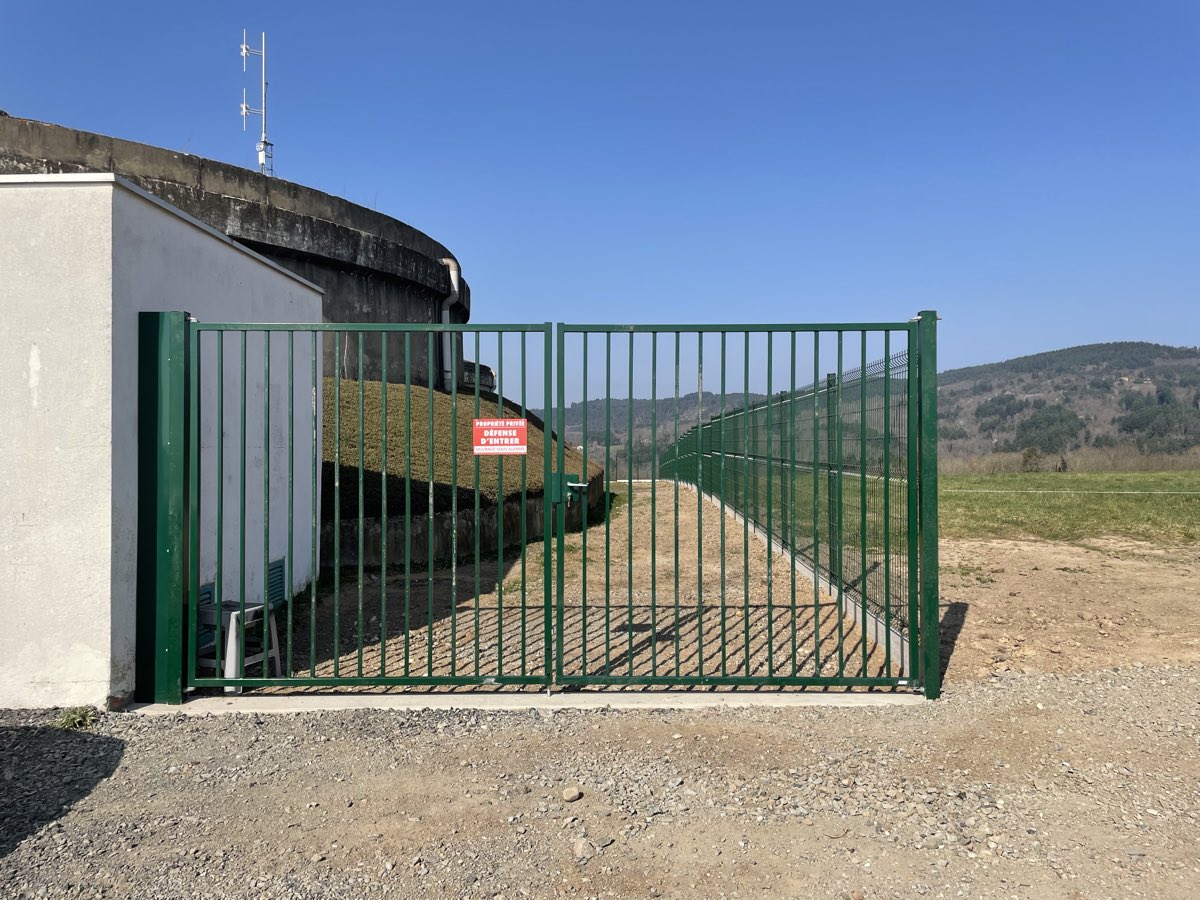 Portail industriel a double battant barreaude de couleur verte avec panneau d'acces interdit, ouvrant sur un site cloture